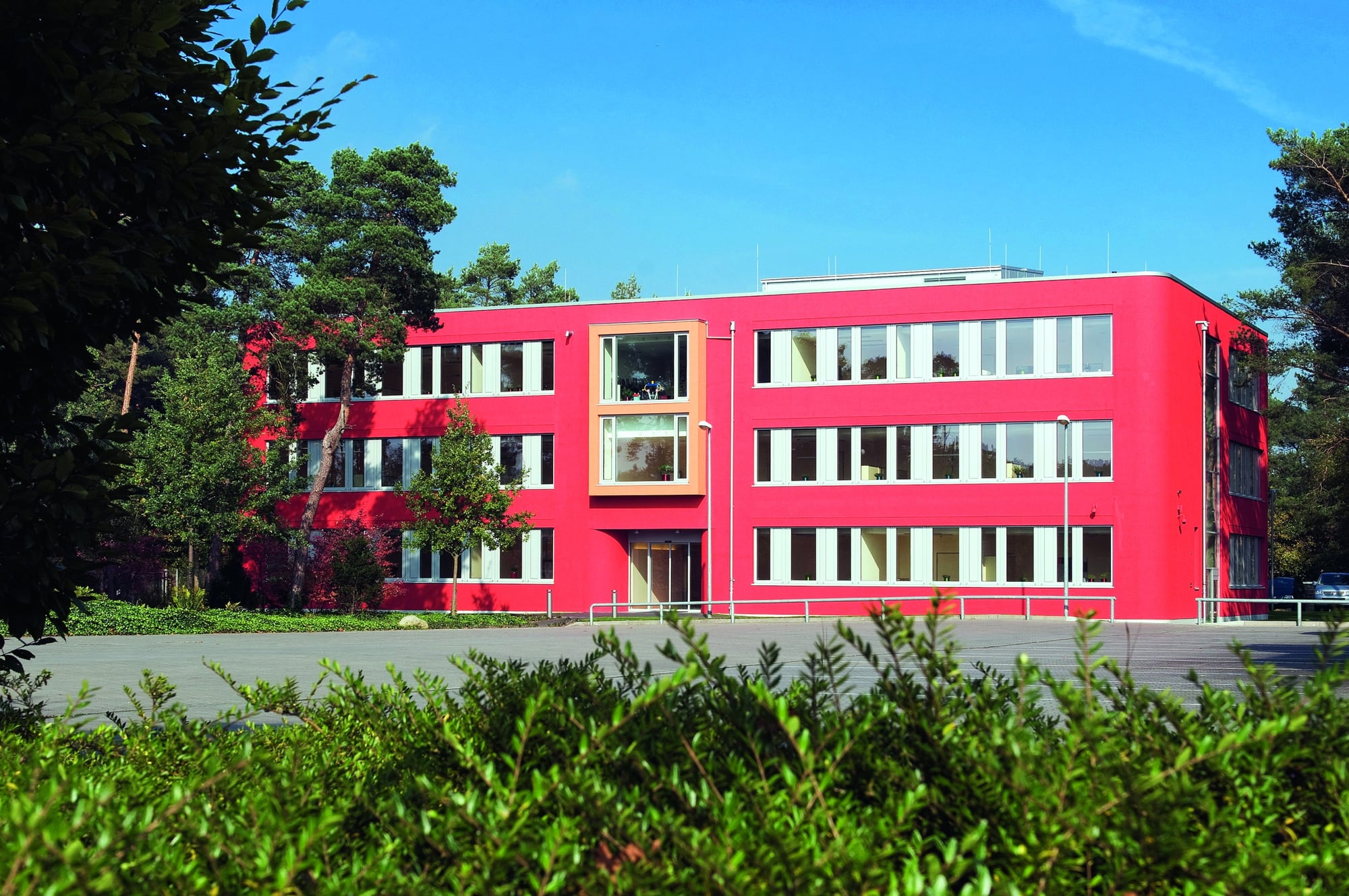 Firmengebäude von Naber: ein rot verkleideter Bürobau hinter einer Hecke, mit begrünter Fassadenseite