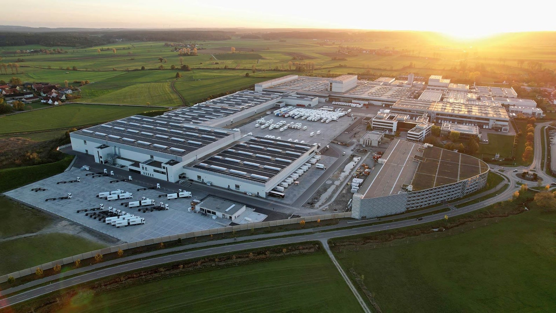 Luftbild des Schüller-Werks bei tief stehender Sonne: ausgedehnte Produktionshallen mit Photovoltaik auf den Dächern, ringsum Felder
