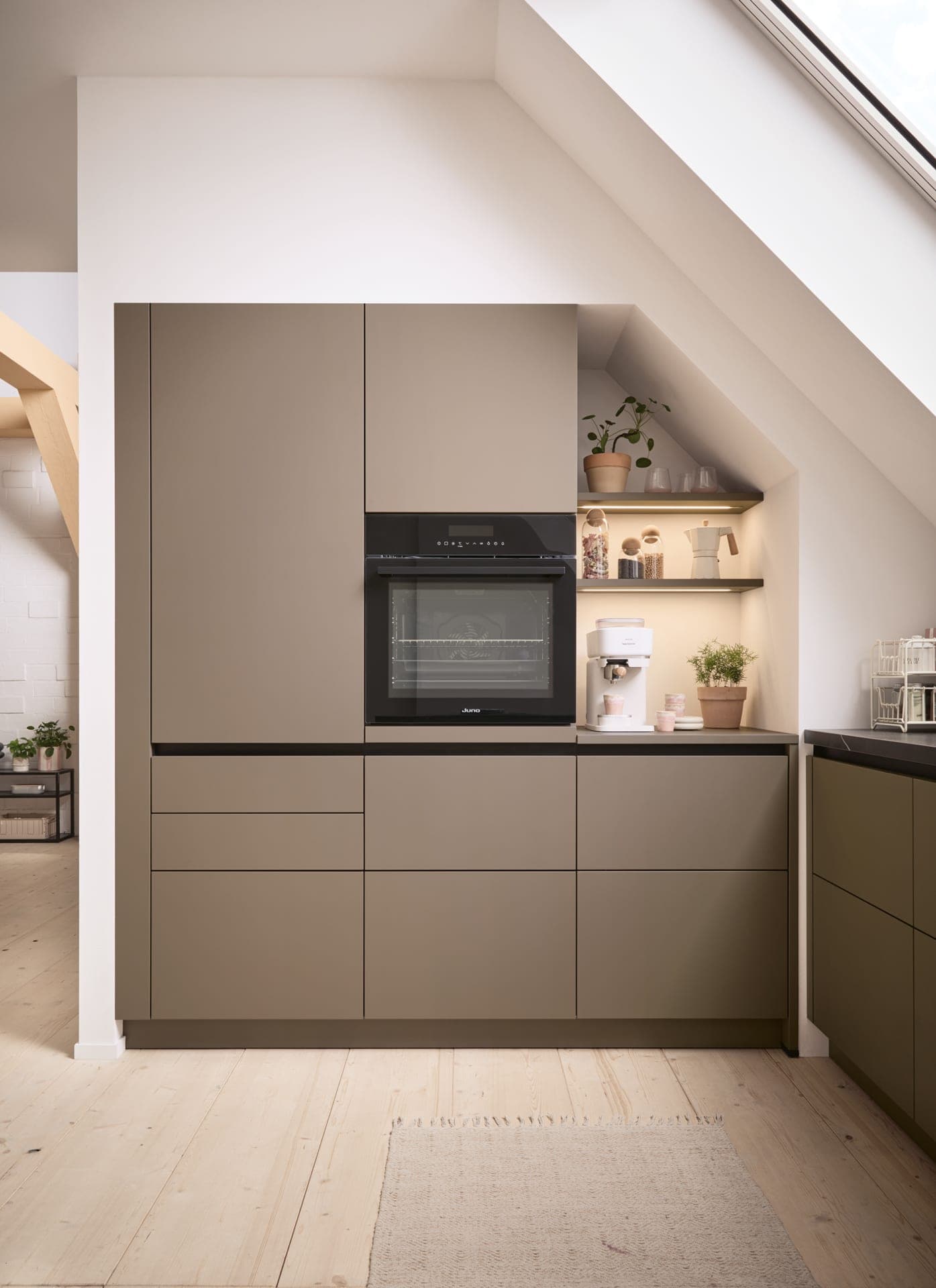 Grifflose Küche in warmem Taupe mit beleuchteten Eichennischen und Backofen auf Sichthöhe
