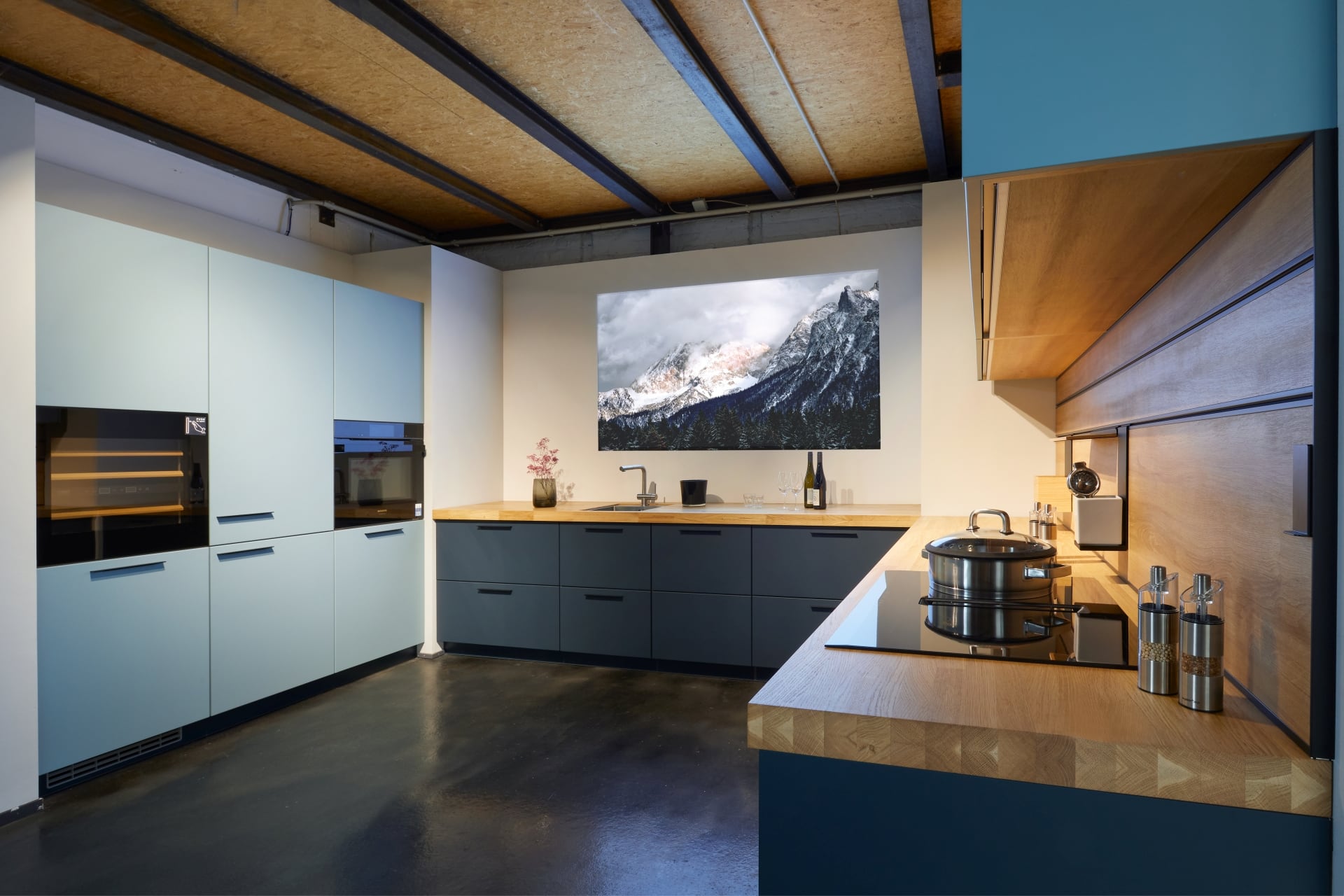 Ausstellungsküche im KüchenLoft Köln: Hochschränke in Hellblau, Unterschränke in dunklem Blau, Arbeitsplatte aus Eiche, darüber die Holzdecke auf Stahlträgern