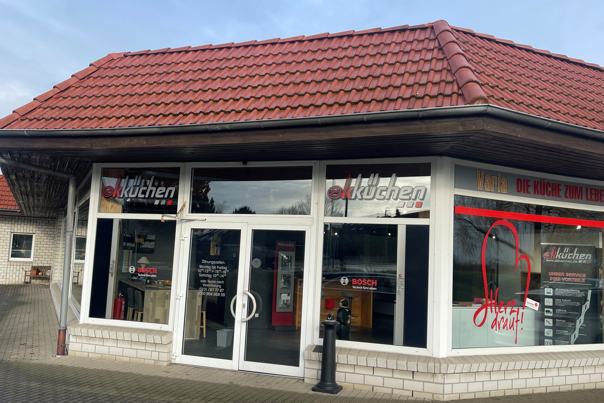 Das Küchenstudio in Lünen-Brambauer von außen: rotes Ziegeldach, Glastür in der Mitte, Schaufenster mit Herz und dem Schriftzug der Arbeitsplatten