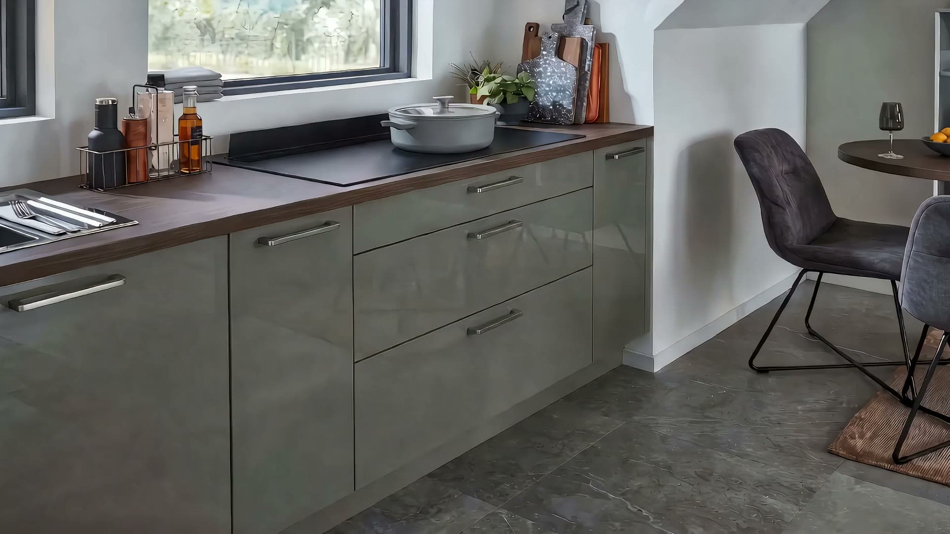 Eine breite Schublade in einer graugrünen Küche gleitet ganz auf, darin Vorratsdosen, Schneidebretter und Teller