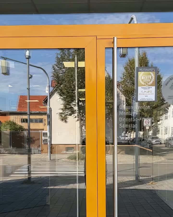 Rundgang durch das Küchenstudio in Karlsdorf: durch die orange gerahmte Glastür hinein, an der weißen Küchenzeile und der Musterwand entlang, vorbei an der Kochinsel unter der grünen Decke und am runden Tisch bis zur dunklen Küche an der blauen Wand