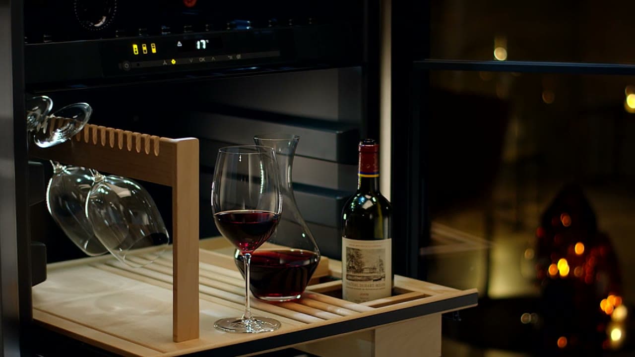 Ausgezogene Schublade im Weinschrank mit Glashalter, einem Glas Rotwein, Karaffe und Flasche
