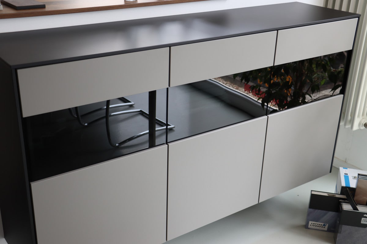 Sideboard mit hellgrauen Fronten ohne Griffe, schwarzer Abdeckplatte und einem Band aus dunklem Glas in der Mitte